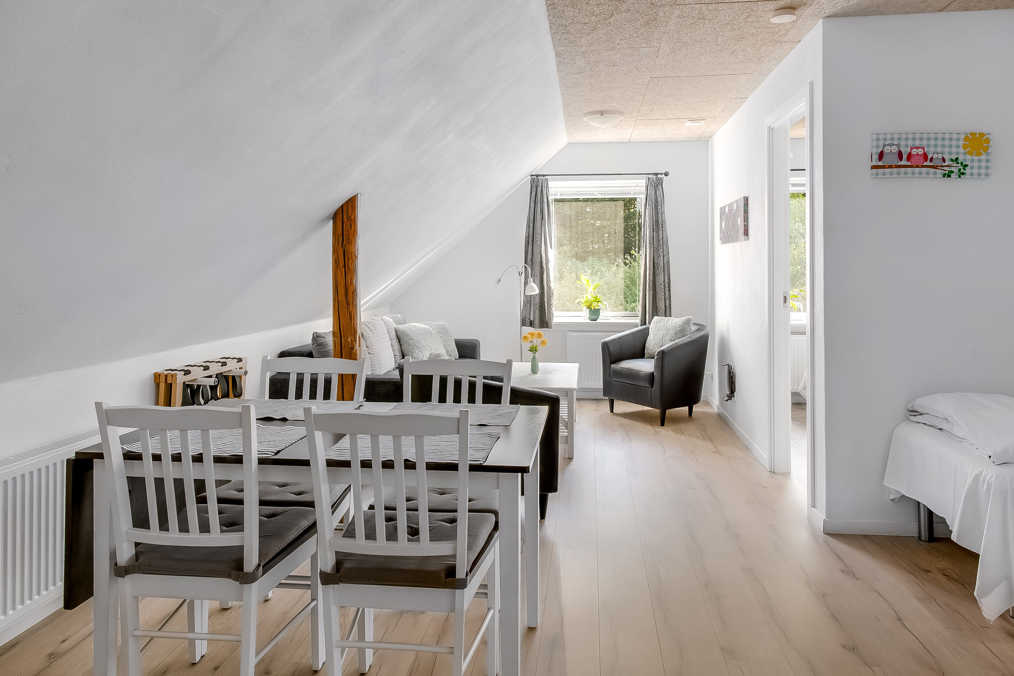Ferielejlighed, opholdsstue med spiseplads med fire stole. Bagerst er der magelige møbler
