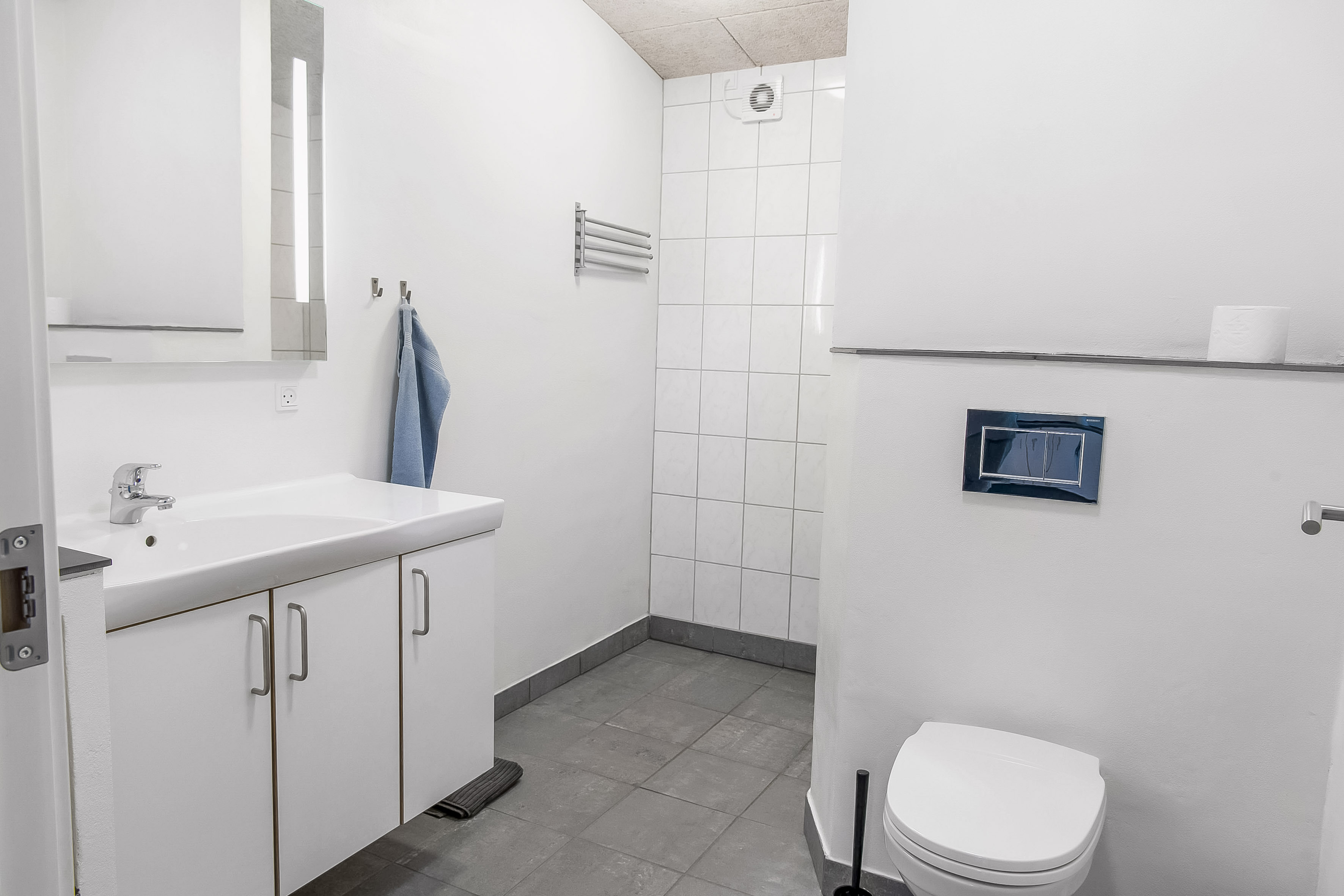 Stor ferielejlighed - her er badeværelse med skabe, spejl, toilet og bruseniche 