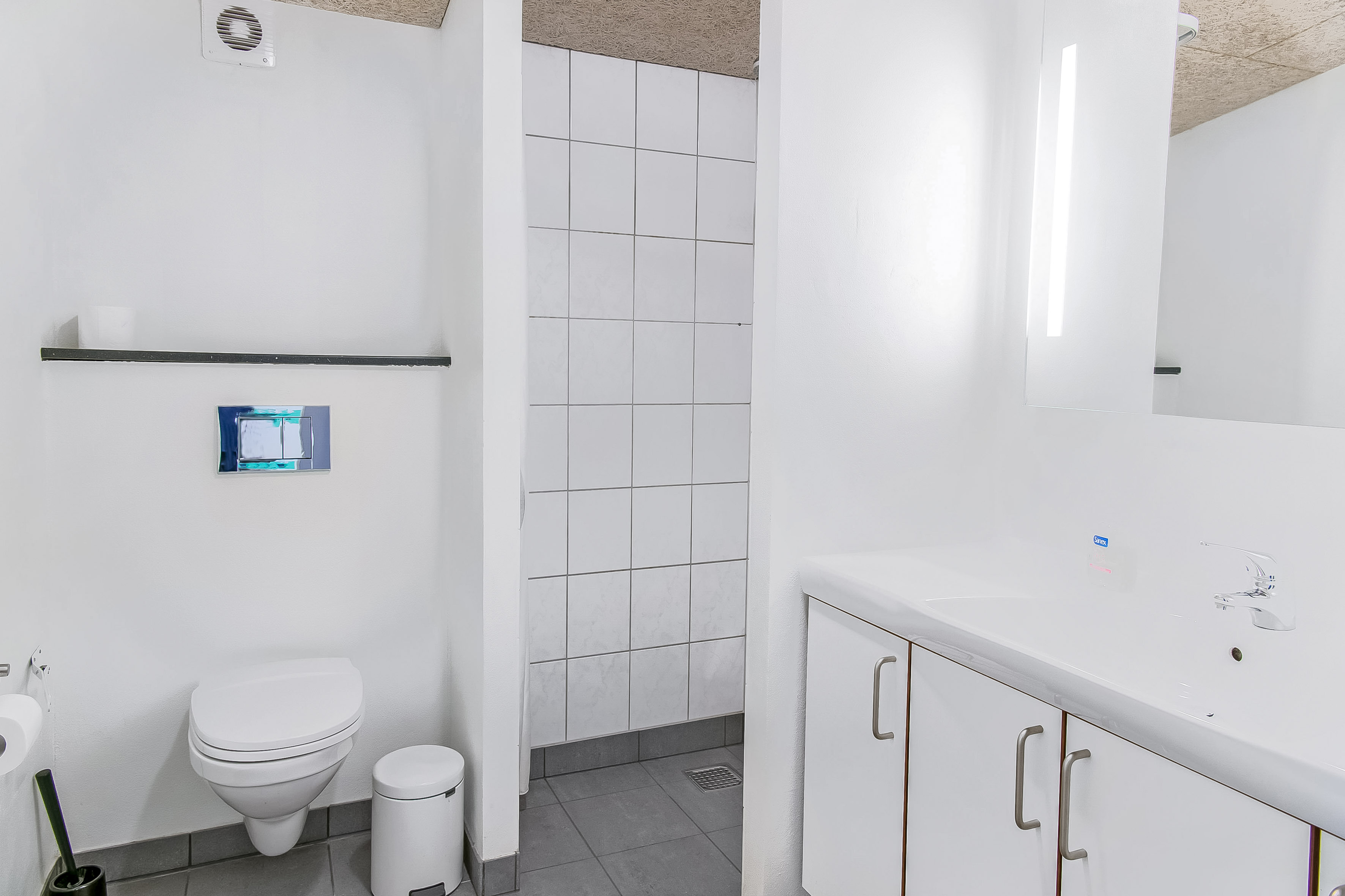 Ferielejlighed, badeværelse med toilet, badeværelsesskabe, bruseniche og spejl med lys