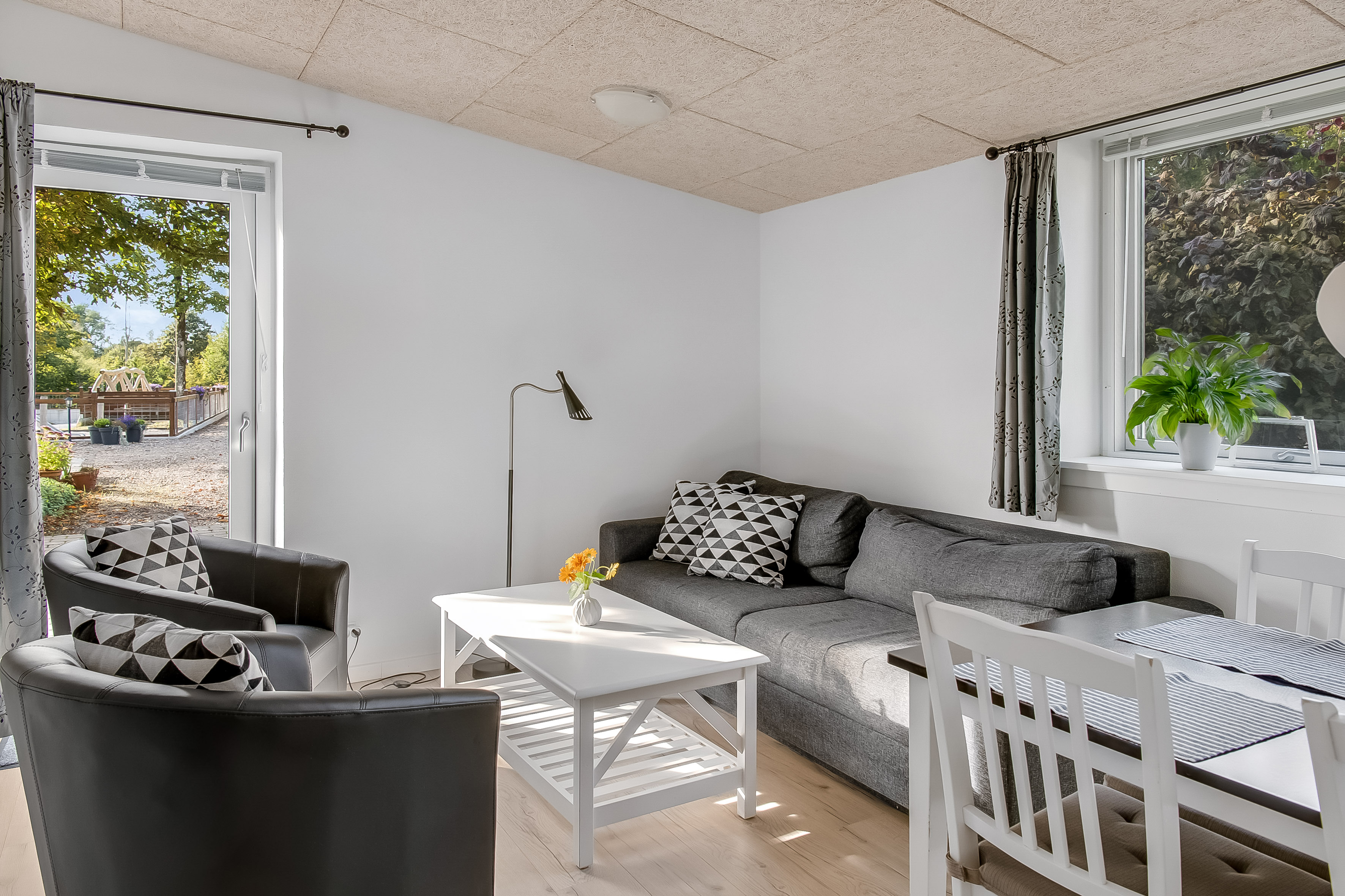 Ferielejlighed, opholdsstue med dobbelt sovesofa, magelige møbler og spiseplads. Dør ud til terrassen.