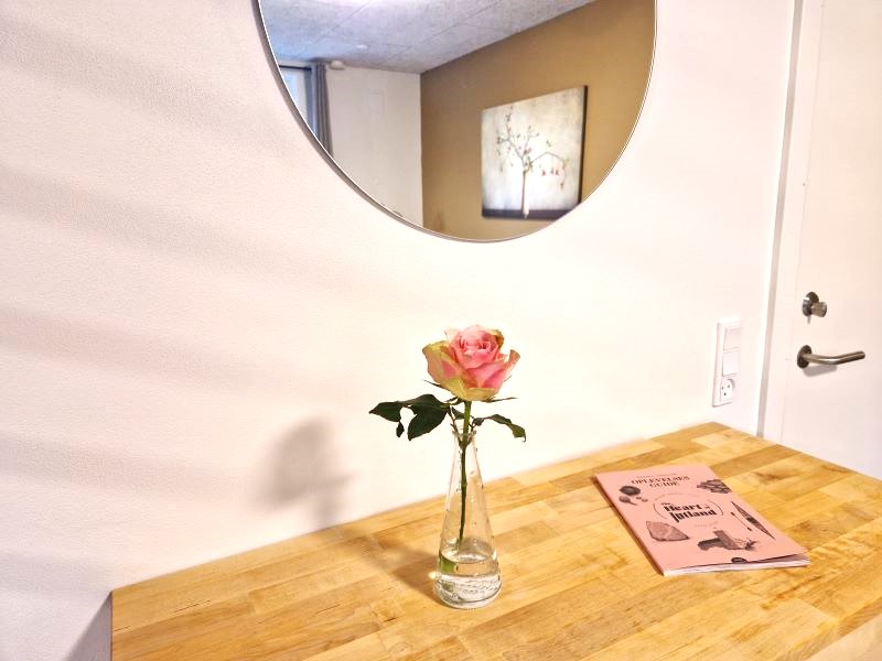 Detalje fra Hemse-stuen, vase med rose, rundt spejl og opslagsbog